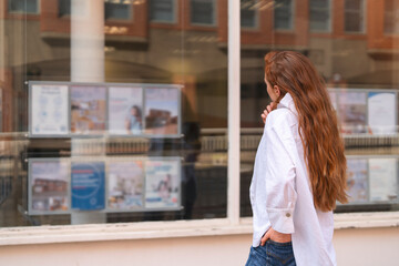 Young woman looking at real estate listings in a window display in an urban setting during the day