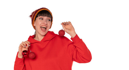 Cheerful woman wearing a red hoodie and colorful beanie holds Christmas ornaments while celebrating the holiday spirit