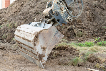 Closeup of an excavator bucket of an excavator doing earthwork.  Pile of earth in the background.