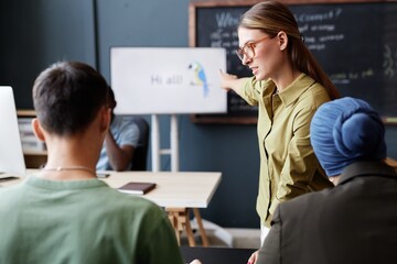 Professional female English language instructor discussing with adult students homework pointing at...