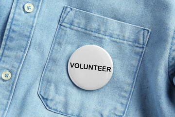 Button badge with word Volunteer attached to denim shirt, closeup