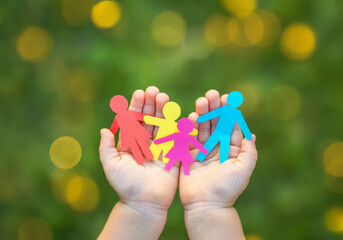 Hands of a Child Holding Paper Figures Depicting Love, Happy Families, and Volunteerism for a Better Society