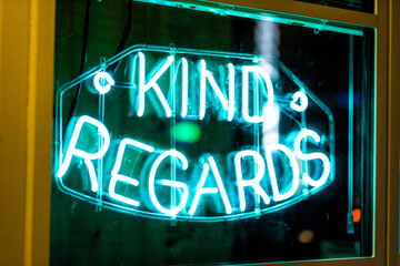 Neon Sign Displaying 'Kind Regards' Glowing in Vibrant Teal, Captured at Night in a Window Setting,...