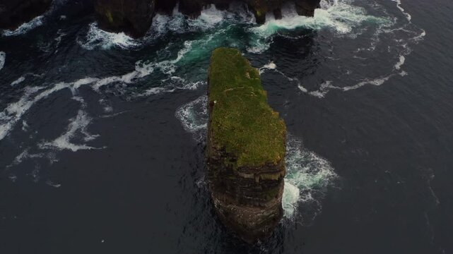Aerial pullback and tilt up of Dun Briste sea stack at Downpatrick Head, rises to reveal grassy landscape