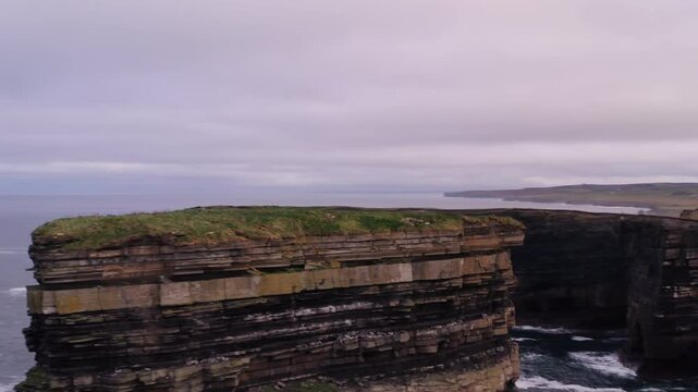Aerial orbit of Dun Briste sea stack with Downpatrick Head coastline behind revealing waves crashing on rocks