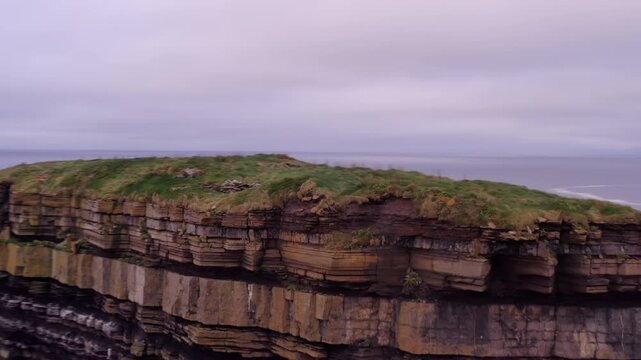Medium telephoto aerial orbit and pullback from layered stacked rocks of Dun Briste sea stack at Downpatrick Head Ireland