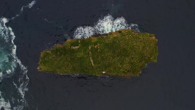 Aerial top down static of Dun Briste sea stack surrounded by ocean waves as seagulls soar as white dots above vegetation