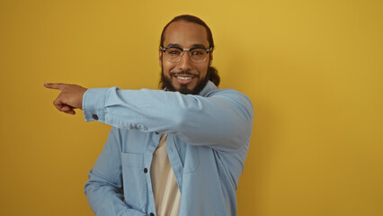 Young man with beard wearing glasses pointing confidently over yellow background