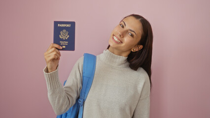 Young woman holding an american passport smiling against a pink background, showcasing her...