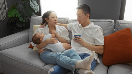 Family relaxing in a cozy living room with mother holding baby while father drinks coffee, showcasing a loving chinese couple and their toddler in a warm apartment setting.