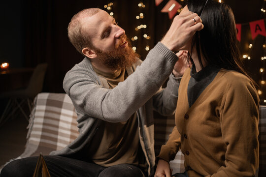 Young couple preparing to celebrate birthday party at home. Husband helping wife to put party hat on her head. Birthday preparation - Powered by Adobe