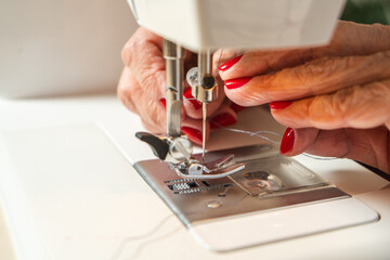 Hands of an older woman threading the sewing machine needle before starting.