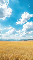 Obraz premium A serene landscape featuring golden fields under a bright blue sky with fluffy clouds and distant mountains.