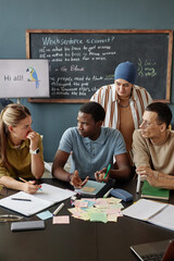 Vertical shot of young Black man talking to female teacher sitting at desk in group discussion,...