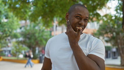 Young man smiling in urban park setting with trees in the background during a sunny day, capturing a lively outdoor ambiance of the city street.