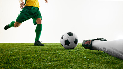 Single bombardier in green uniform running towards ball on field on green soccer stadium, while goalkeeper on ground against white studio background. Concept of sport event, championship, match. Ad