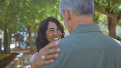 Fototapeta premium Man and woman enjoying a romantic moment in a sunny outdoor urban park, showcasing love and connection during middle age while surrounded by nature and smiling warmly.
