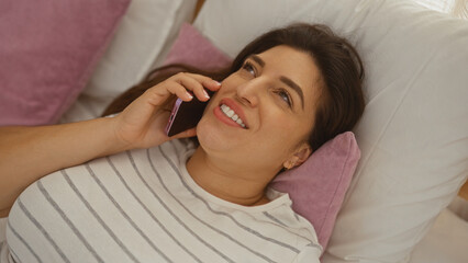 Woman lying on a couch talking on her smartphone and smiling in a cozy living room