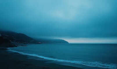 Serene coastal landscape at dusk with fog and gentle waves.