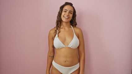 Fototapeta premium Beautiful young hispanic woman smiling on an isolated pink background wearing a white bikini