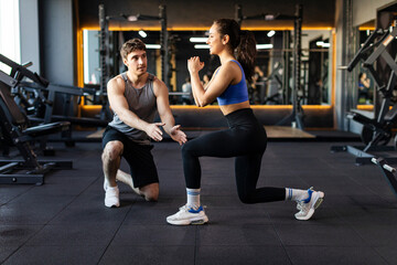 Personal male trainer controlling woman client and talking how to do lunges correctly while...