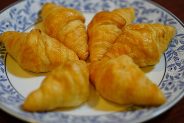 Five pieces of butter croissants on a white plate with a blue pattern.