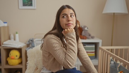 Woman sitting in bedroom next to cradle with thoughtful expression, surrounded by toys in a cozy...