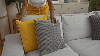 Woman arranging yellow and gray pillows on a modern gray sofa in a cozy, home interior