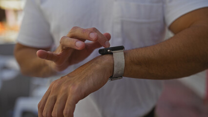A hispanic man adjusts his smartwatch on an urban street while outdoors, captured in a detailed portrait of his hands and wrist in a city setting.
