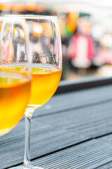 Two Glasses of Sparkling White Wine on a Wooden Table Outdoors, With a Colorful and Blurred Background of a Bustling Market or Street Festival Scene