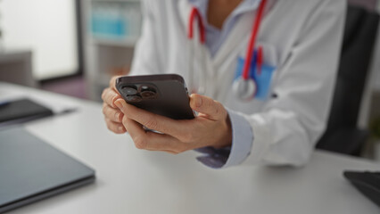 Woman using smartphone in clinic setting, dressed in white coat, suggesting medical professional environment with focus on hands and mobile device interaction.