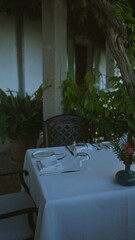 Outdoor restaurant table set for two with white tablecloth and flowers, surrounded by lush greenery in mallorca, spain.