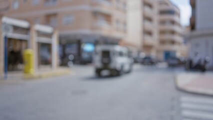 Blurred city street scene with a white van driving through an urban area in daylight with out-of-focus buildings and pedestrians in the background.