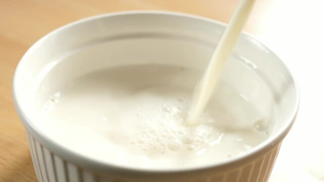 pouring milk into an empty white bowl