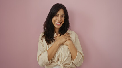 Young, beautiful, hispanic woman standing over an isolated pink background with a joyful smile and hands clasped near her chest, conveying warmth and happiness.