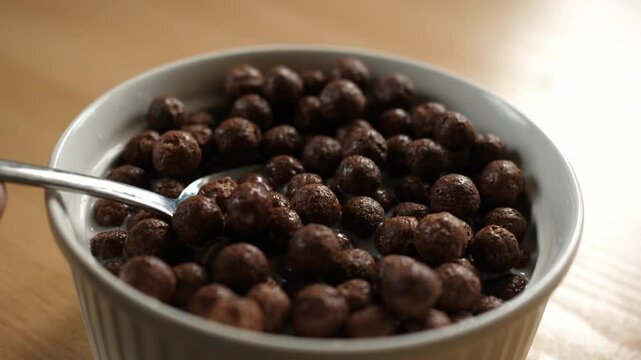 slow motion scooping chocolate choco cereal balls with a spoon from a bowl full of milk