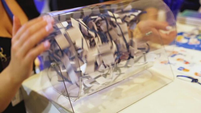 Process of prize drawings, extracting a winning numbers of lottery machine, raffle drum with a bingo balls, bingo machine and winning tickets on event with a female host, hands on lottery machine