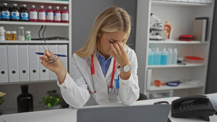 Woman doctor sitting stressed in a clinic holding glasses resting amid medical equipment indicating...