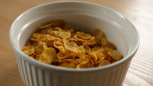 pouring cornflakes into an empty white bowl