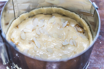 Raw apple tart with almond petals in a baking dish on the production table