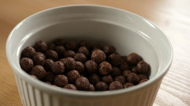 pouring brown chocolate choco cereal balls into an empty white bowl