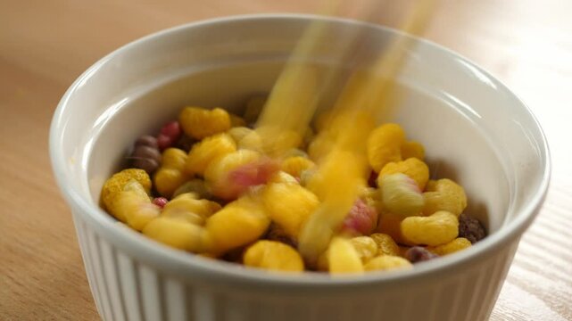 pouring colorful fruity cereal into an empty white bowl