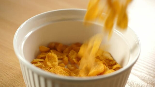 slow motion pouring cornflakes into an empty white bowl