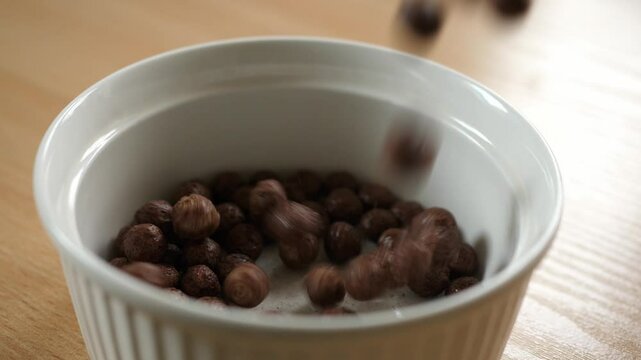 slow motion pouring brown chocolate choco cereal balls into an empty white bowl