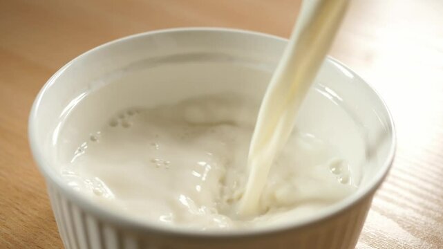slow motion pouring milk into an empty white bowl