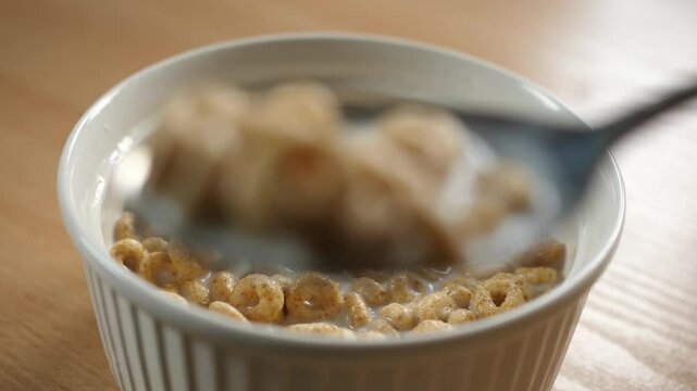 scooping honey cereal rings with a spoon from a bowl full of milk