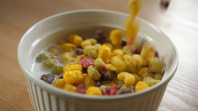 slow motion pouring colorful fruity cereal into an empty white bowl