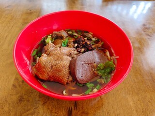 Braised duck noodles in bright red bowl on woood table.