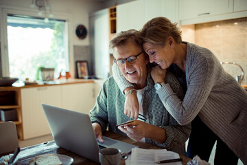 Happy senior couple online shopping on laptop from home kitchen