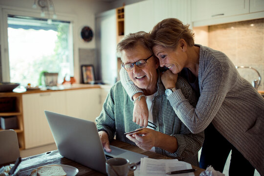 Happy senior couple online shopping on laptop from home kitchen